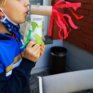 Slika prikazuje dečka, ki piha v zmaja narejenega iz tulcev za straniščni papir.