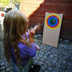 Slika prikazuje deklico, ki strelja v pisano tarčo.